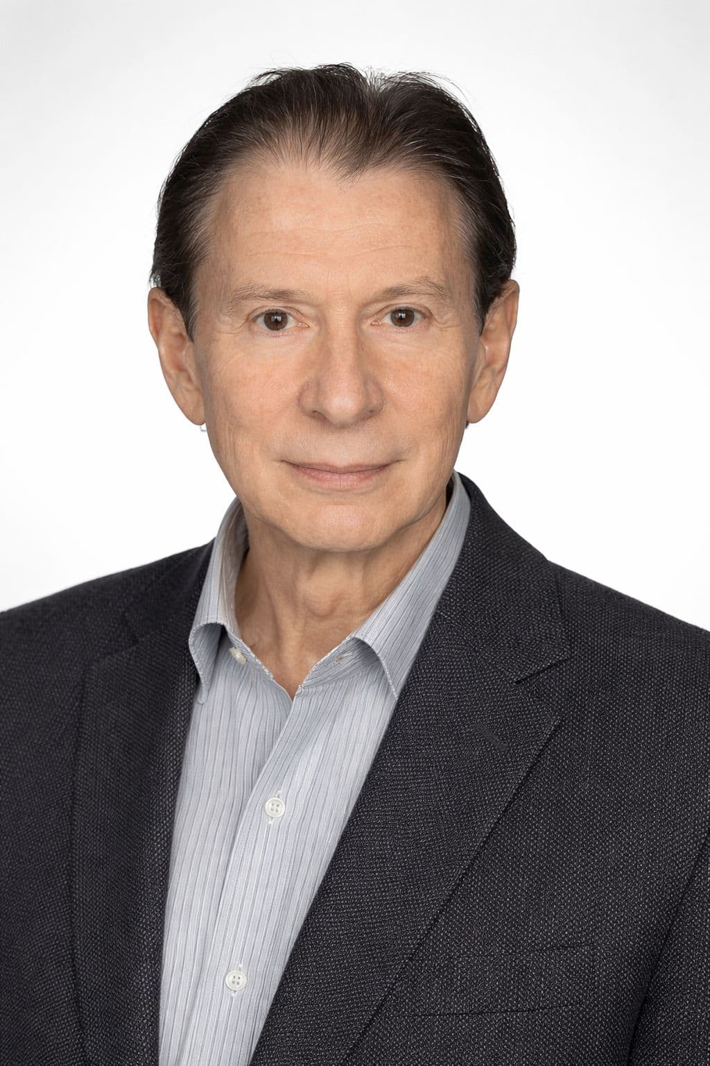 Middle-aged man with dark hair wearing a grey blazer and striped shirt against white background.